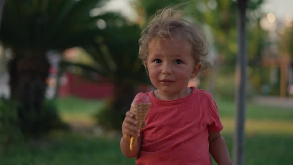 Fairhaired Boy Eats White Cold Cream Ice Cream in Waffle Cone Cup While Sitting Outside in Sunny