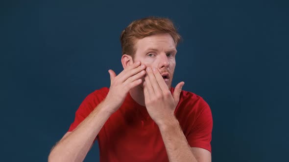 Young Man Examining His Skin Problems Looking at Camera Over Dark Blue Background