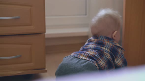 Little Boy in Shirt and Pants Crawls on Floor in Light Room