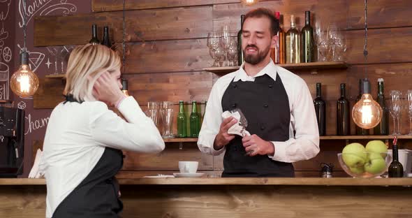 Bartender Cleans a Glass and Listens Very Concentrated To His Female Coworker