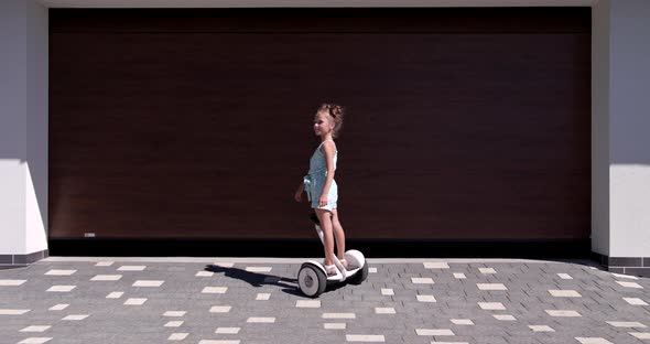 Little Girl Rides A Gyroscooter Near The Garage