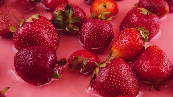 Falling strawberries into the water on a pink background. Slow motion.