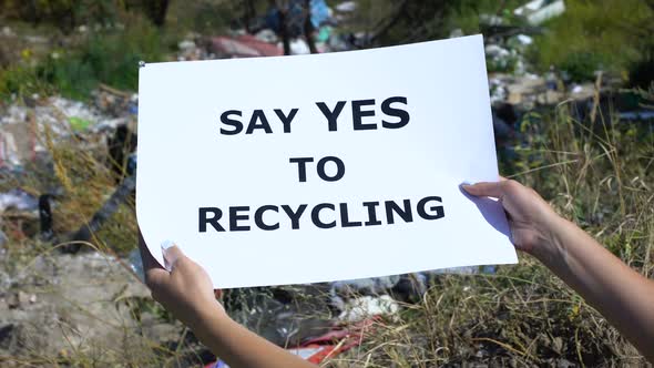 Say Yes to Recycling Phrase on Cardboard in Hands Against Landfill Background