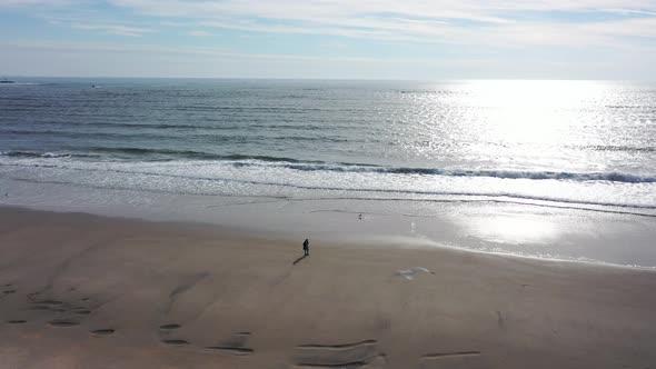 An aerial view of a quiet beach with one person walking in the morning. The camera truck right and p
