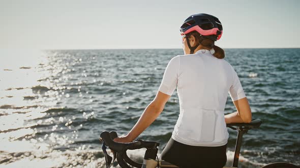 Woman in Protective Helmet Sunglasses and Sportswear is Sitting on Trekking Bike Nearby a Sea