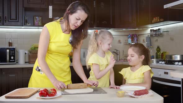 Mom Cook Rolls Out the Dough on the Table. Mom with Children in the Kitchen Preparing To Eat