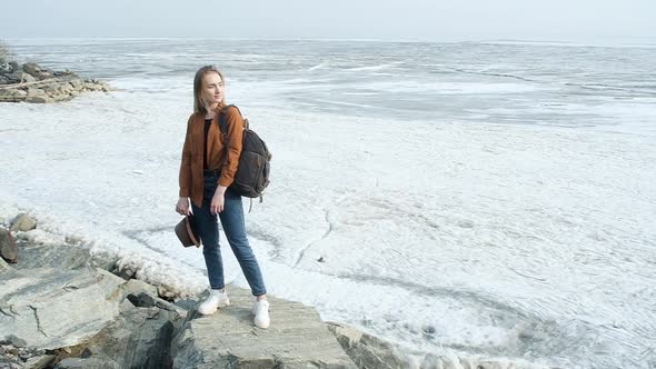 female alone with backpack stands on stone cliff by sea and  and enjoys vacation