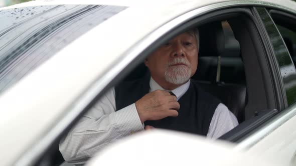 4K Senior businessman sitting in the car straightens his shirt and necktie before driving.