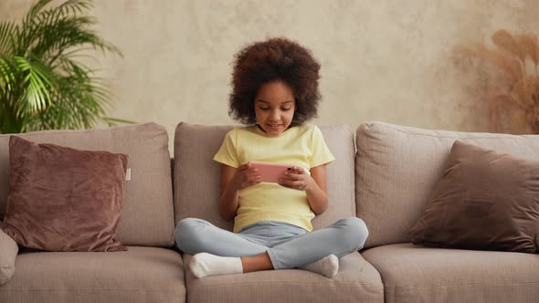 Portrait Little African American Girl in Plays a Game on Smartphone