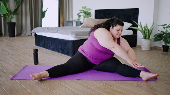 Young Overweight Woman Stretches Body Sitting on Mat at Home