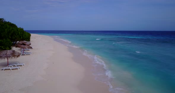 Daytime drone tourism shot of a white sandy paradise beach and blue water background in vibrant 4K