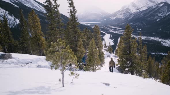 The Stunning Banff Alpine Views in Stormy Winter as Two Young Hikers Explore Snow and Green Pine Tre