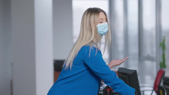 Gorgeous Slim Young Woman in Coronavirus Face Mask Disinfecting Hands with Sanitizer in Office