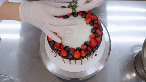 Closeup of a Pastry Chef Decorating a Cake with Strawberries with Mint Leaves