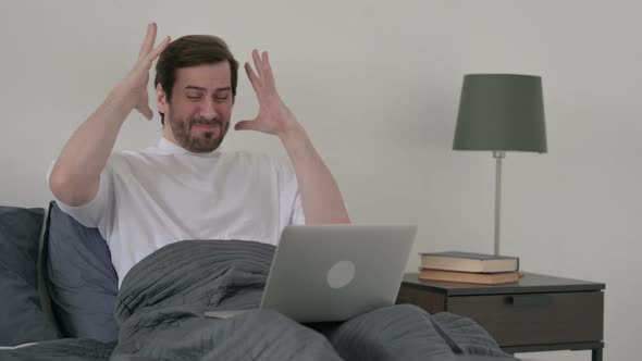 Young Man Reacting to Loss on Laptop in Bed