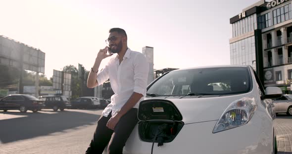 Young Man Using Mobile Phone While Charging an Electric Car