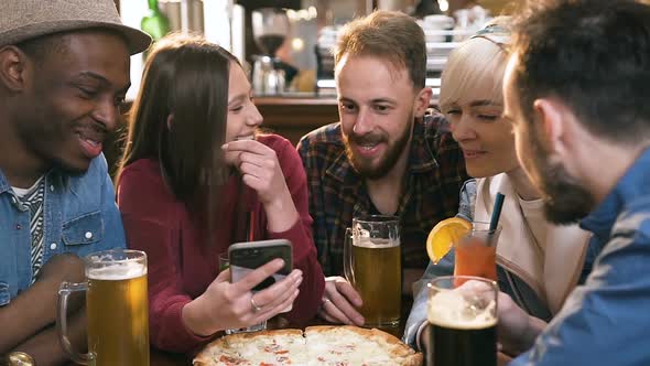 Company of Multi Ethnic Friends Watching Video, Photo on the Smart Phone in the Modern Bar