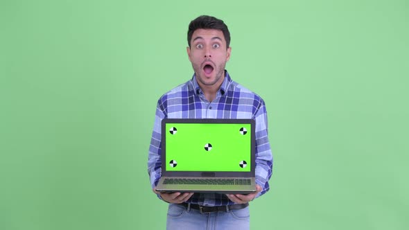 Happy Young Hispanic Man Showing Laptop and Looking Surprised