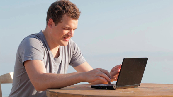 Man Typing on a Small Laptop Computer