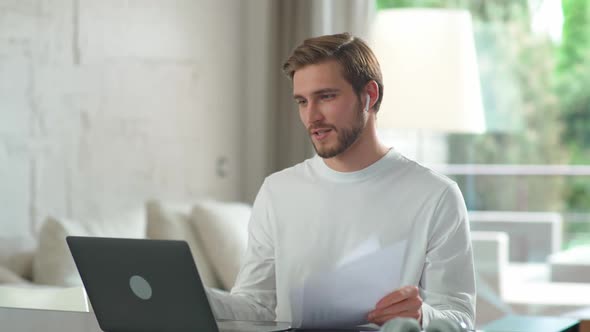 Caucasian Man Wearing Wireless Headphones Communicates with Colleagues By Video Call Using a Laptop