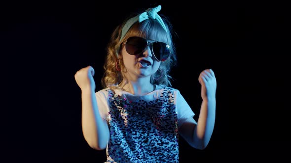 Trendy Girl in Futuristic Glasses Dancing Listening To Music in Headphones on Black Background