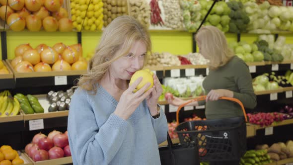 Portrait of Positive Caucasian Senior Woman Smelling Fresh Organic Pear and Smiling at Camera