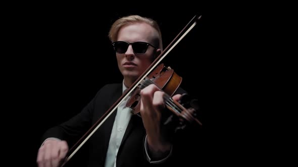 Young Caucasian Male in Black Suit and Glasses Plays Violin on Dark Background