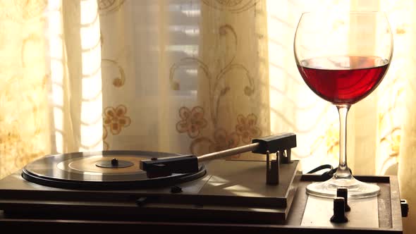 Red Wine and Vintage Vinyl Record on Gramophone By Curtains
