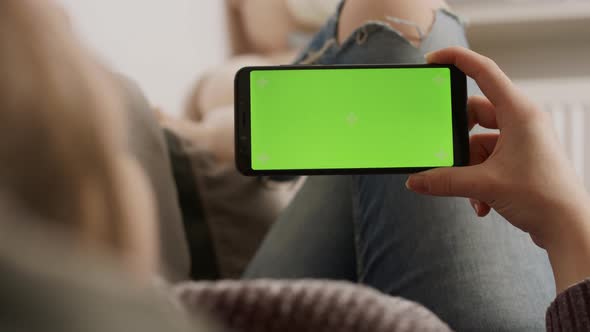 Young Woman Holding Smartphone with Green Screen While Resting on the Sofa and Waving. Video Call