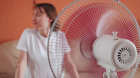 Young Woman Sits in Front of Electric Home Fan Air Stream Blowing Short Hair