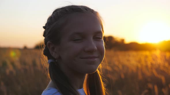 Portrait of Happy Smiling Girl Looking Into Camera Against Background of Grass Field