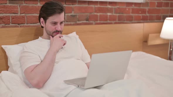 Young Businessman Thinking and Working on Laptop in Bed