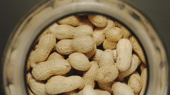 TOP VIEW: Unpeeled Peanuts Fall Into Glass Jar - Slow Motion