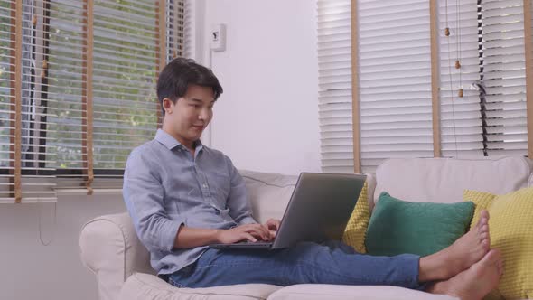 At home, a business asian man types and works online on a desk table with a laptop.
