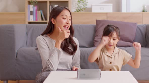 Happy asian mother and daughter sing a song and dancing together watching music video apps in smartp