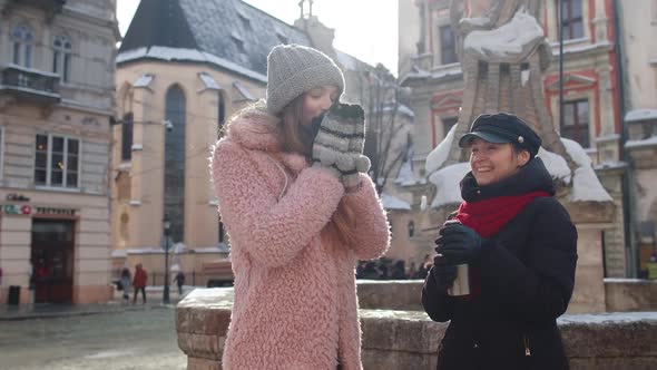 Two Smiling Women Tourists Traveling Together Drinking Hot Tea Coffee From Thermos on City Street