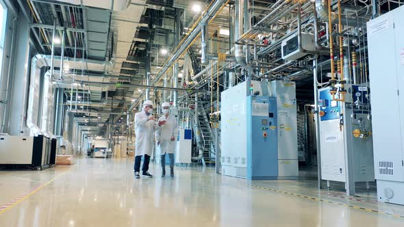 Two Specialists in Face Masks are Walking Through the Factory Unit