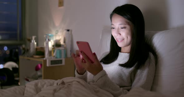 Woman look at mobile phone on bed at night