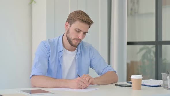 Pensive Young Creative Man Writing on Paper Thinking