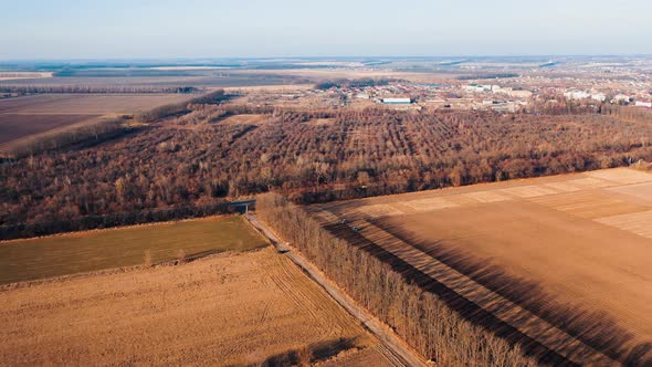 View of autumn farm fields, forest and road with cars. Aerial landscape of agriculture.