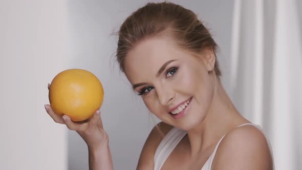 Happy Woman Smiling and Playing with Orange Near Face