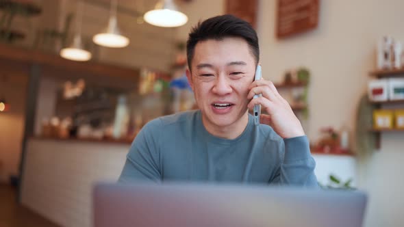 Smiling Asian young man working by laptop and talking by phone