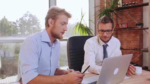 Male Office Worker in Blue Shirt Explaining Prokect at Laptop to His Caucasian Boss in Glasses Anf