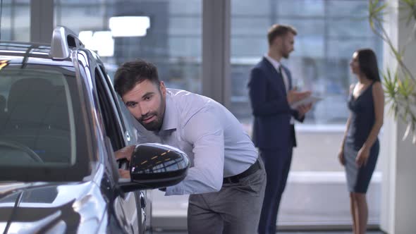 Joyful Male Buyer Looking Inside Car at Dealership