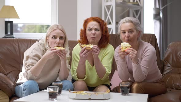 Portrait of Three Absorbed Women Eating Pizza Watching TV Resting on Weekend at Home in Living Room