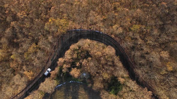 Aerial view of a white car driving through orange autumn countryside at sunse