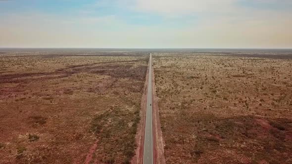 AERIAL LOWERING - A lone car travels through the vast, deserted Australian Outback