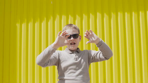 Boy in Sunglasses Gesticulates Moves His Hands on Bright Sunny Day
