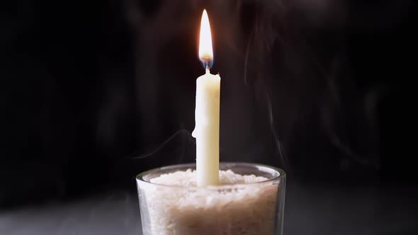 Burning White Candle in a Glass on a Black Background Shrouded in Smoke