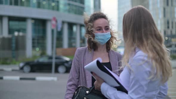 woman in medical mask talking to colleague on the street after working day